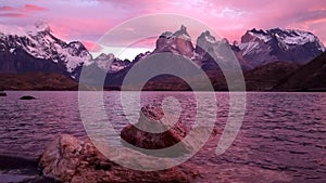 Beautiful pink sunset with view on mountain lake with scenic rocks on first plan in Torres del Paine Park in Patagonia.