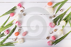Beautiful pink tulips with colorful quail and chicken eggs in nest on white wooden background.