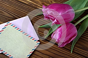 Beautiful pink tulips on wooden background with envelop.Copy space.