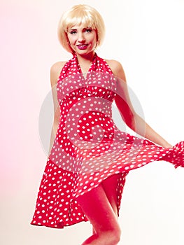 Beautiful pinup girl in blond wig and retro red dress dancing. Party.