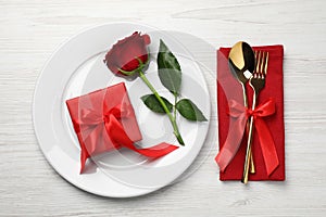 Beautiful place setting with dishware, gift and rose for romantic dinner on white wooden table, flat lay