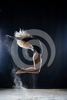 Beautiful plump blonde girl wearing a black gymnastic bodysuit covered with clouds of the flying white powder jumps dancing