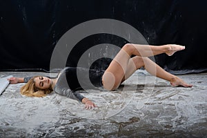 Beautiful plump blonde girl wearing a black gymnastic bodysuit covered with clouds of the flying white powder jumps dancing