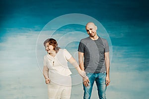 Beautiful plump woman holds the hand of a tall bald man on a blue background.