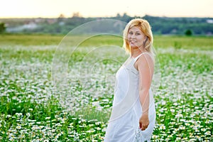 A beautiful plus size girl with white hair in a white summer dress poses outdoors with camomiles. A plump girl in a meadow with