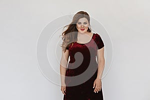 Beautiful plus size model girl in modish red velvet dress isolated at white background. Young fat woman with bright