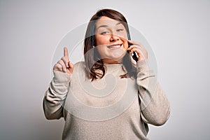 Beautiful plus size woman having a conversation talking on smartphone over isolated background surprised with an idea or question