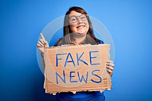 Beautiful plus size woman holding fake news banner for false journalism over isolated background surprised with an idea or