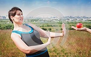 Beautiful plus size woman in sportswear refusing healthy food