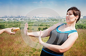 Beautiful plus size woman in sportswear refusing junk food