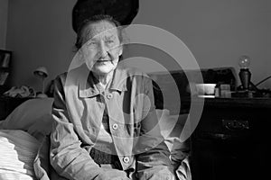 Beautiful 80 plus year old senior woman portrait. Black and white image of elderly worried woman sitting on a bed.