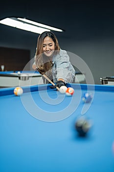 beautiful pool player smiling while poking the billiard ball