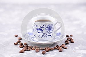 A beautiful porcelain coffee cup with hot black coffee. Coffee beans scattered around the background. Vintage china. A white-blue