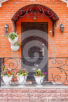 A beautiful porch in a rich house with black door, red brick wall and white flower pots.