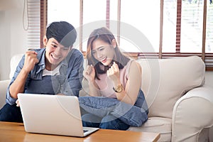 Beautiful portrait asian young couple working laptop with smile and happy sitting on couch at living room