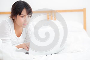 Beautiful portrait asian young woman smile lying on bed using laptop computer with happy at bedroom for leisure and relax