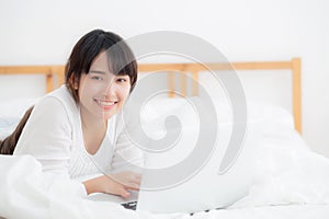 Beautiful portrait asian young woman smile lying on bed using laptop computer with happy at bedroom for leisure and relax