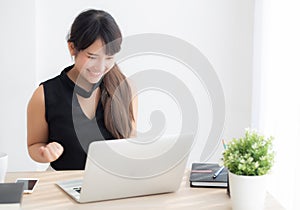 Beautiful portrait asian young woman smile working online laptop computer with happy satisfied sitting on desk office