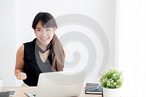 Beautiful portrait asian young woman smile working online laptop computer with happy satisfied sitting on desk office