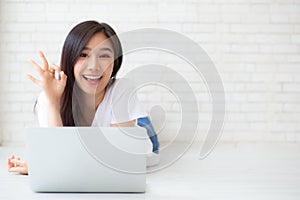 Beautiful portrait asian young woman working online laptop with excited lying on floor brick cement background, freelance girl