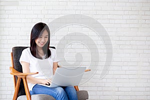 Beautiful of portrait asian young woman working online laptop sitting on chair on cement brick white background