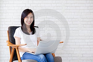 Beautiful of portrait asian young woman working online laptop sitting on chair on cement brick white background