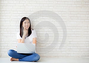 Beautiful of portrait asian young woman working online laptop and thinking sitting on floor brick cement background
