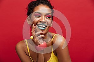 Beautiful portrait of happy african american female model in yellow shirt smiling and posing on camera, isolated over red