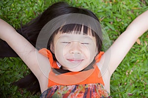 Beautiful portrait little girl asian of a smiling lying on green grass at the park.