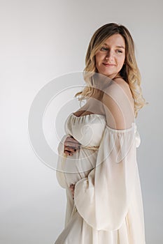 Beautiful portrait of pregnant woman in white dress. Concept of perfect pregnancy. Woman put her hand on belly. Future