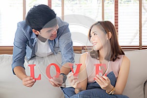 Beautiful portrait young asian couple sitting on sofa holding word love together in living room