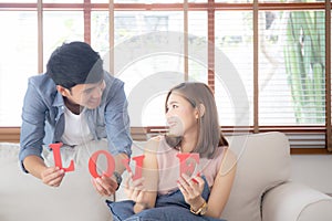 Beautiful portrait young asian couple sitting on sofa holding word love together in living room