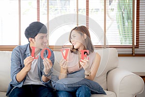 Beautiful portrait young asian couple sitting on sofa holding word love together in living room