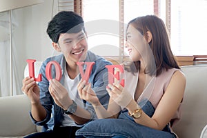 Beautiful portrait young asian couple sitting on sofa holding word love together in living room