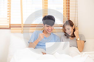 Beautiful portrait young asian couple working laptop with smile and happy sitting in bedroom