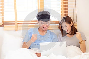 Beautiful portrait young asian couple working laptop with smile and happy sitting in bedroom, man and woman using notebook