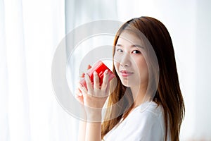 Beautiful of portrait young asian woman with drink acup of coffee standing curtain window background in bedroom