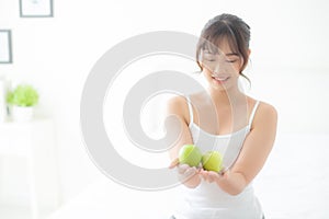 Beautiful portrait young asian woman holding and eating green apple fruit in the bedroom at home