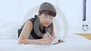 Beautiful portrait young asian woman relax lying on bed thinking idea and writing book or diary