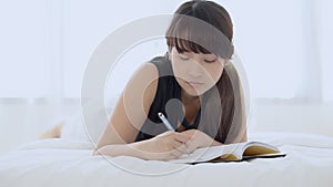 Beautiful portrait young asian woman relax lying on bed thinking idea and writing book or diary in the bedroom at home