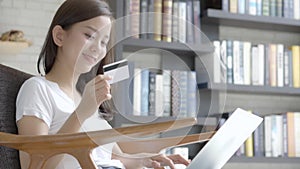 Beautiful portrait young asian woman shopping online with credit card on laptop computer sitting in living room at home