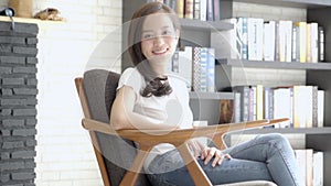 Beautiful portrait young asian woman sitting on chair with smile and happy at living room, moving panning camera