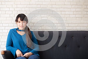 Beautiful portrait young asian woman sitting and smiling happy and looking at camera on sofa with casual at living room