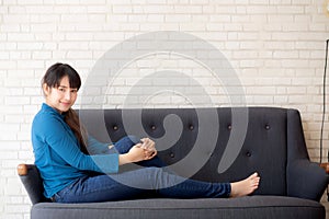 Beautiful portrait young asian woman sitting and smiling happy and looking at camera on sofa with casual at living room