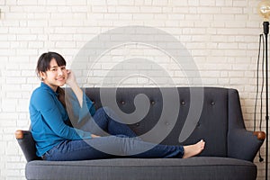 Beautiful portrait young asian woman sitting and smiling happy and looking at camera on sofa with casual at living room