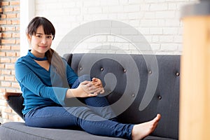 Beautiful portrait young asian woman sitting and smiling happy and looking at camera on sofa with casual at living room