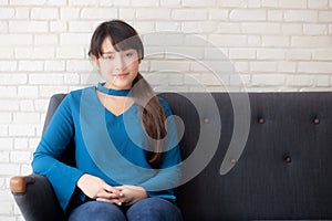 Beautiful portrait young asian woman sitting and smiling happy and looking at camera on sofa with casual at living room