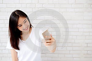 Beautiful portrait young asian woman taking a selfie with smart mobile phone on concrete cement white background