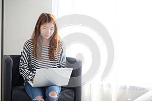 Beautiful of portrait young asian woman using laptop computer for leisure on chair at living room