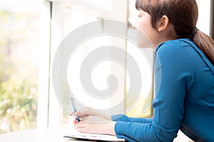 Beautiful portrait young asian woman writer smiling thinking idea and writing on notebook or diary with happy